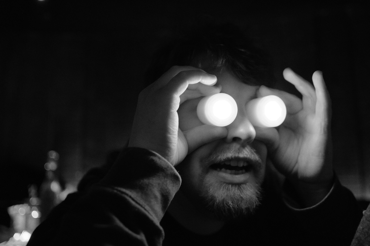 Black and white portrait of a person holding two LED candles in front of their eyes